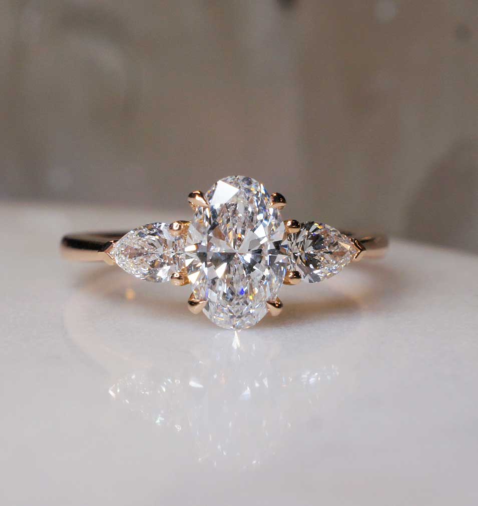 A three stone diamond engagement ring with an oval centre diamond and pear cut diamonds, in rose gold, by Sydney jeweller Lizunova