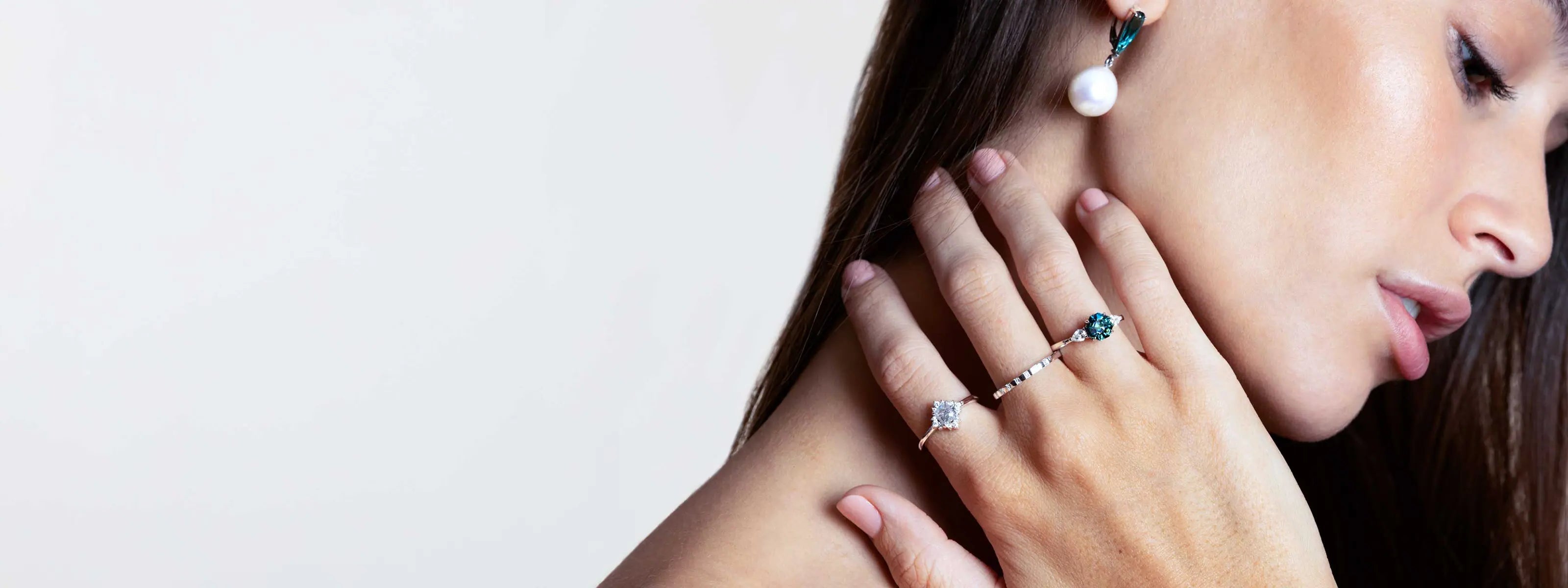 An elegant young female model wearing a sapphire and diamond engagement ring, a wedding band with diamonds, and a white gold salt and pepper diamond engagement ring on her fingers, and pearl and tourmaline earrings, by Australian jeweller Lizunova Fine Jewels, Sydney