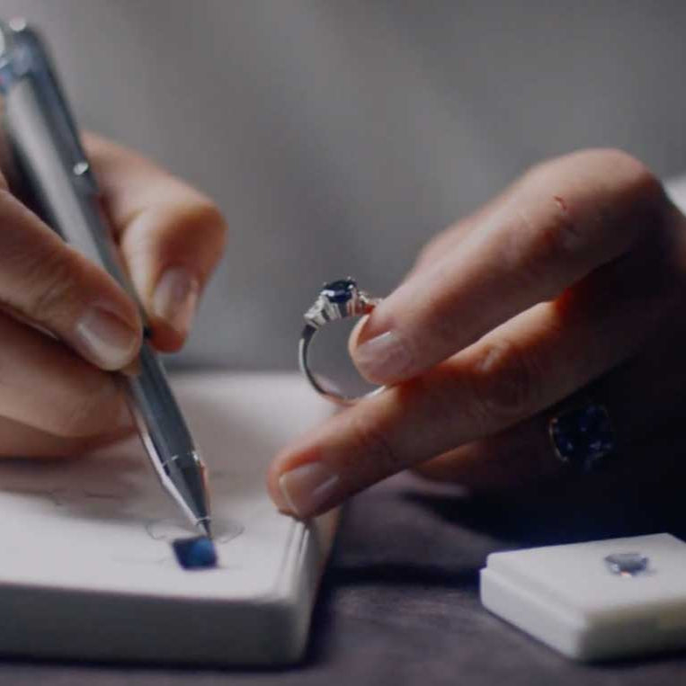 Bespoke Australian jewellery designer Maria Lizunova, of Lizunova Fine Jewels, sketching custom engagement ring designs, with loose sapphires and diamonds on the desk.
