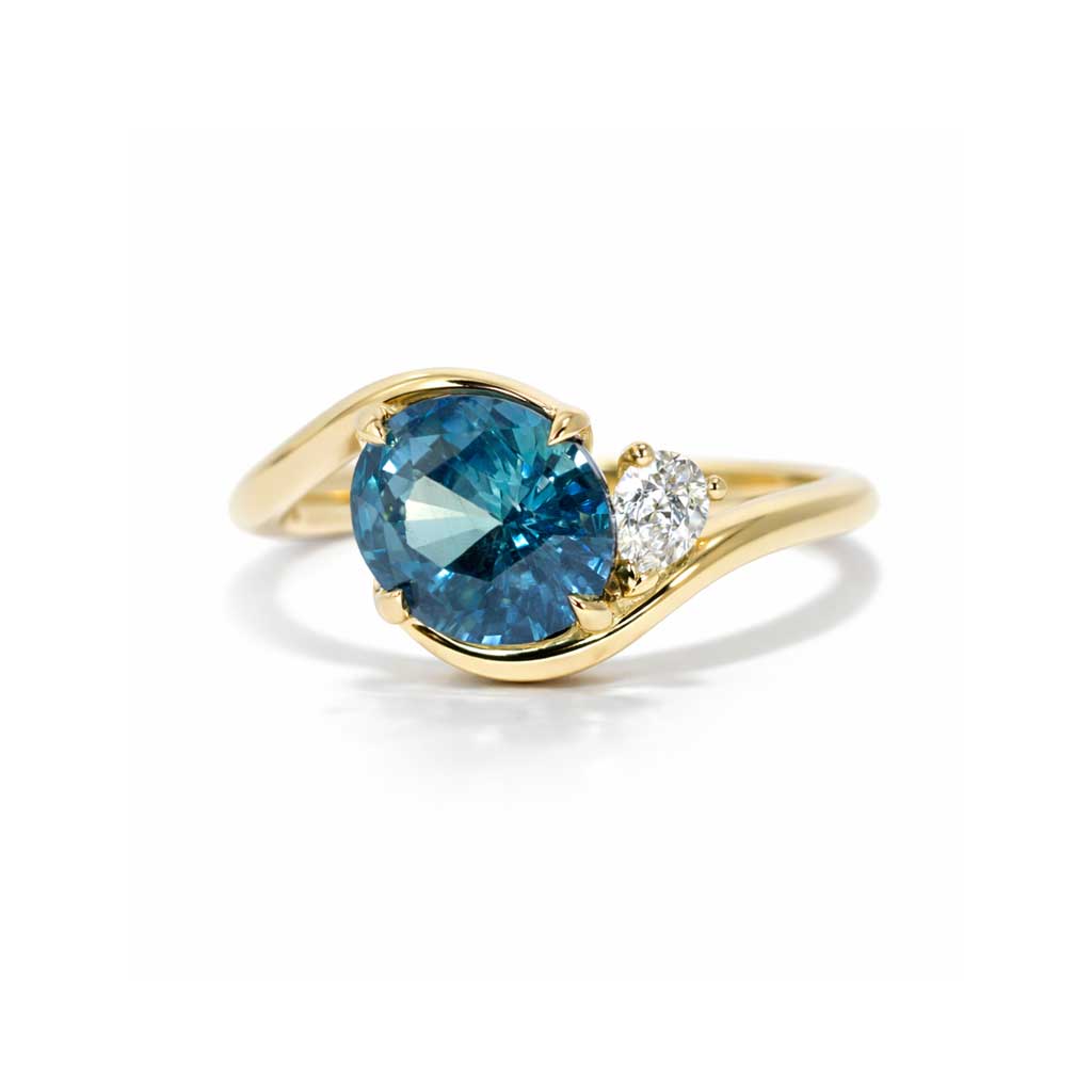 Asymmetric sapphire and diamond engagement ring in 18k yellow gold featuring an oval teal sapphire and sculptural bypass design