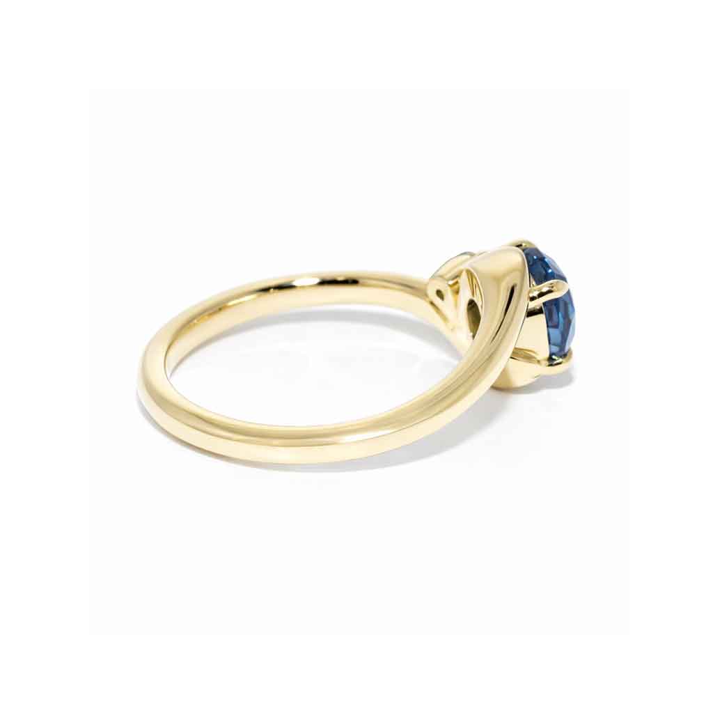 Asymmetric sapphire and diamond engagement ring in 18k yellow gold featuring an oval teal sapphire and sculptural bypass design