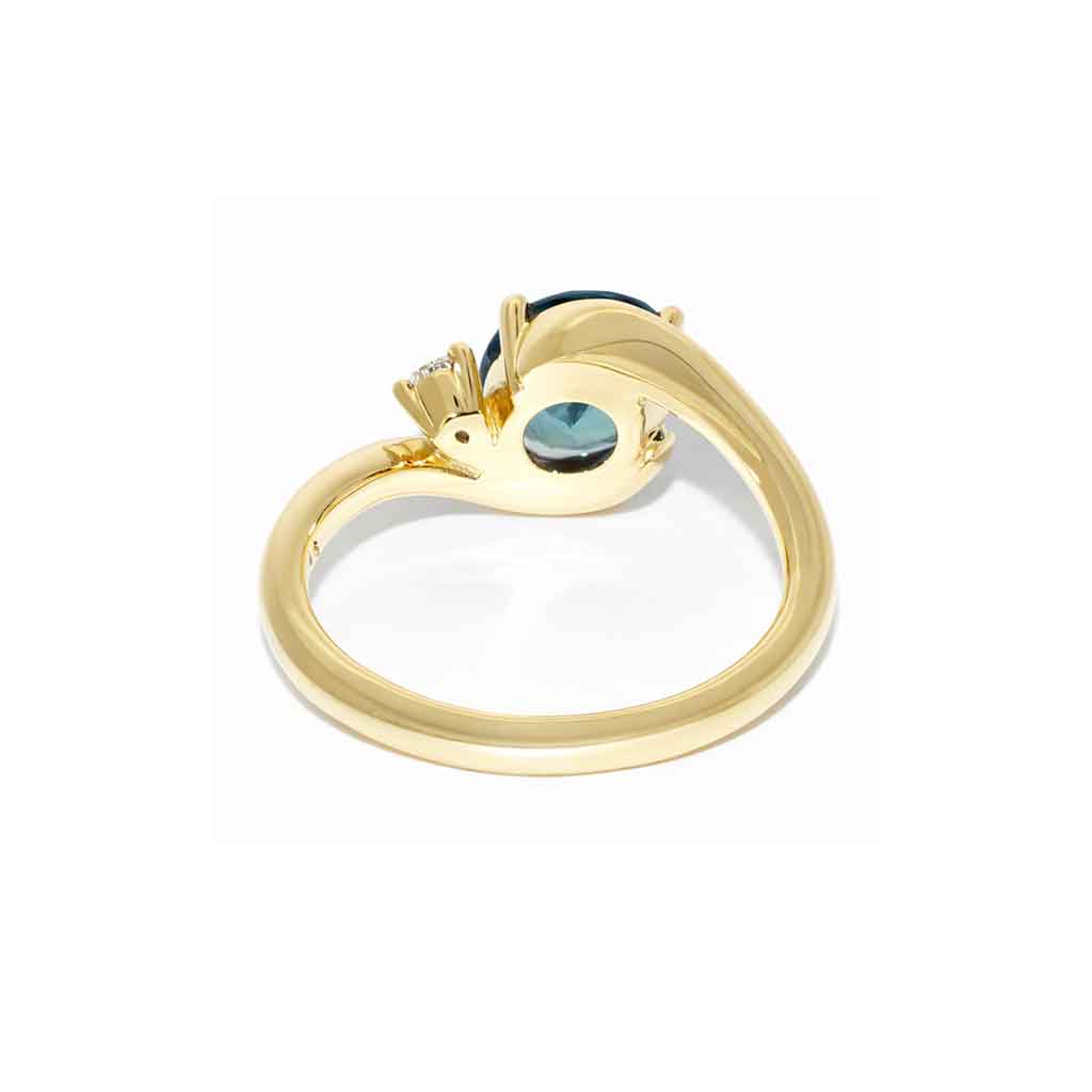 Asymmetric sapphire and diamond engagement ring in 18k yellow gold featuring an oval teal sapphire and sculptural bypass design